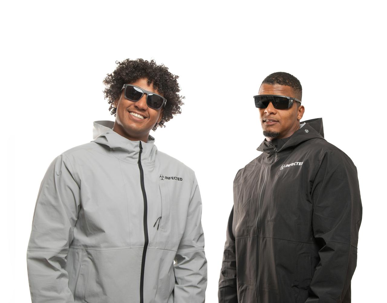 Home Two men in trendy jackets and sunglasses posing confidently against a white background.