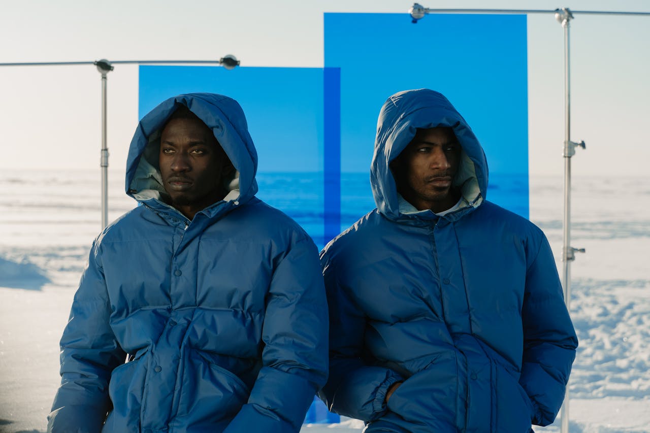 Two men pose in blue jackets against a snowy outdoor backdrop.